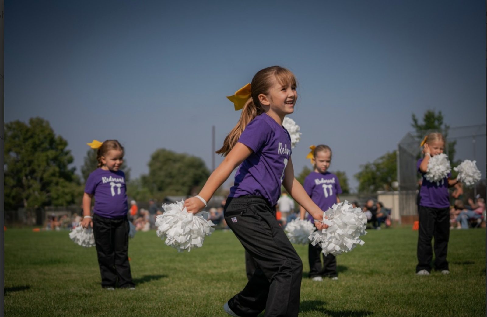 Mini cheerleader smiling and cheering with poms at a game