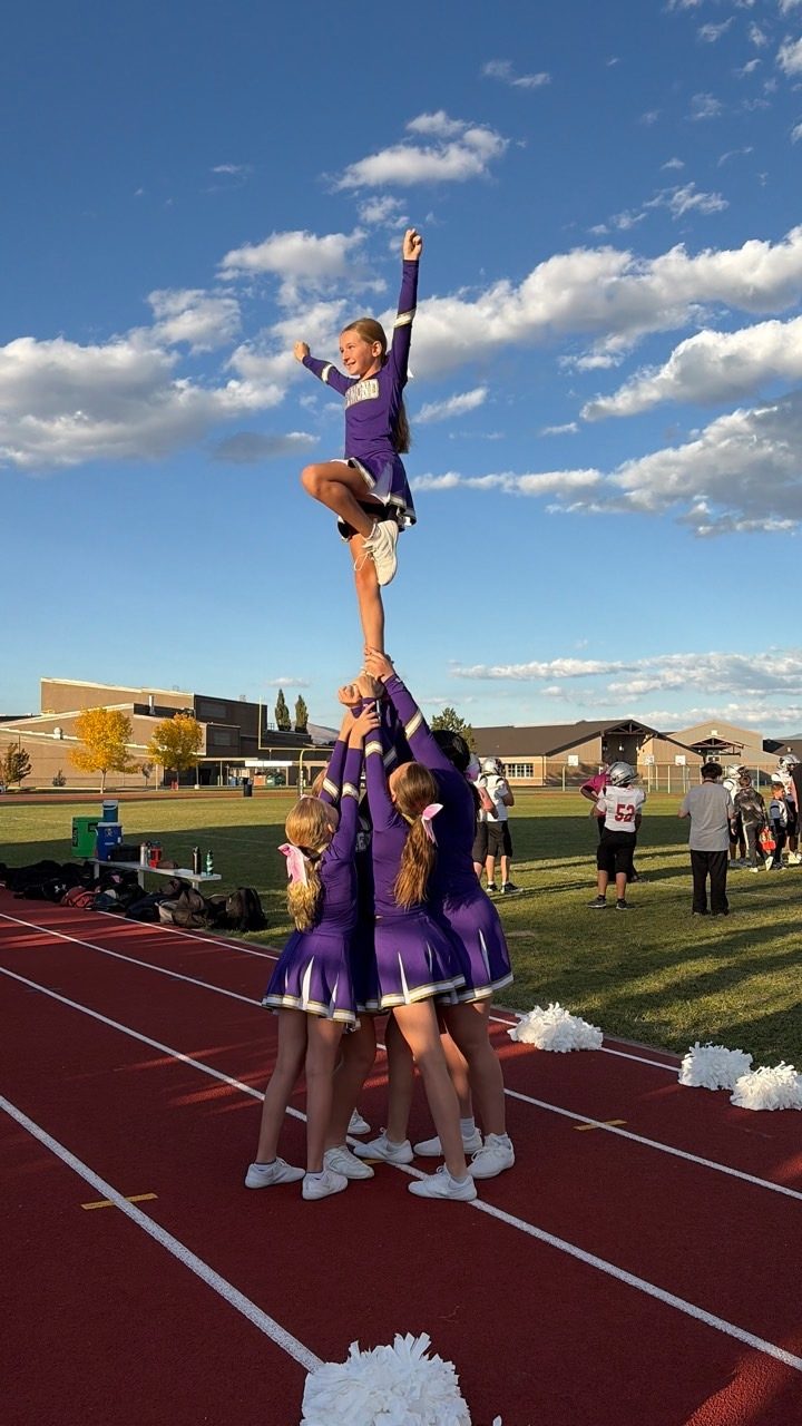 Cheerleader held high in a sideline stunt against a blue sky
